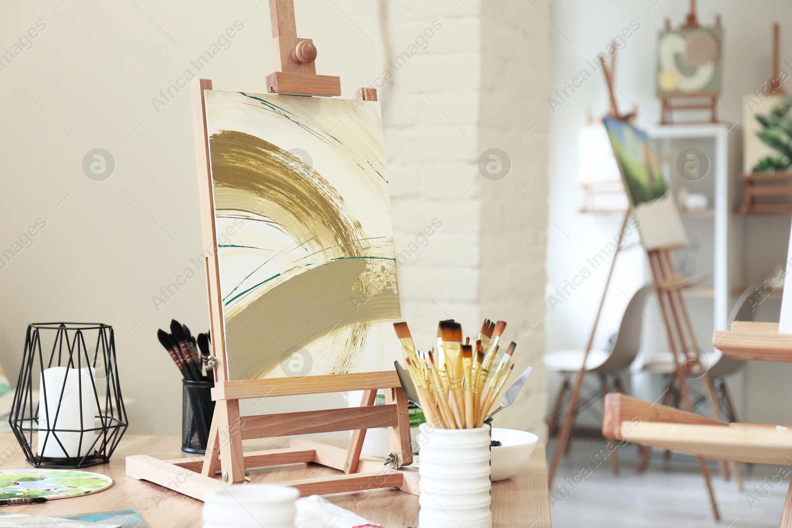 Photo of Small easel with abstract picture and art supplies on table in drawing studio