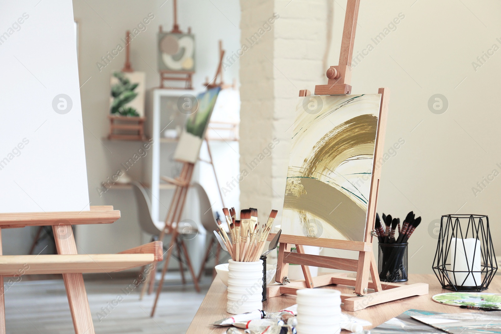 Photo of Small easel with abstract picture and art supplies on table in drawing studio