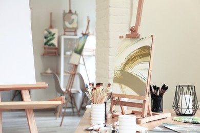 Small easel with abstract picture and art supplies on table in drawing studio