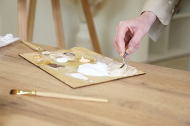 Woman with palette knife at wooden table in drawing studio, closeup