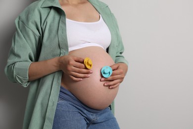 Photo of Pregnant woman with pacifiers on light gray background, closeup and space for text. Expecting twins