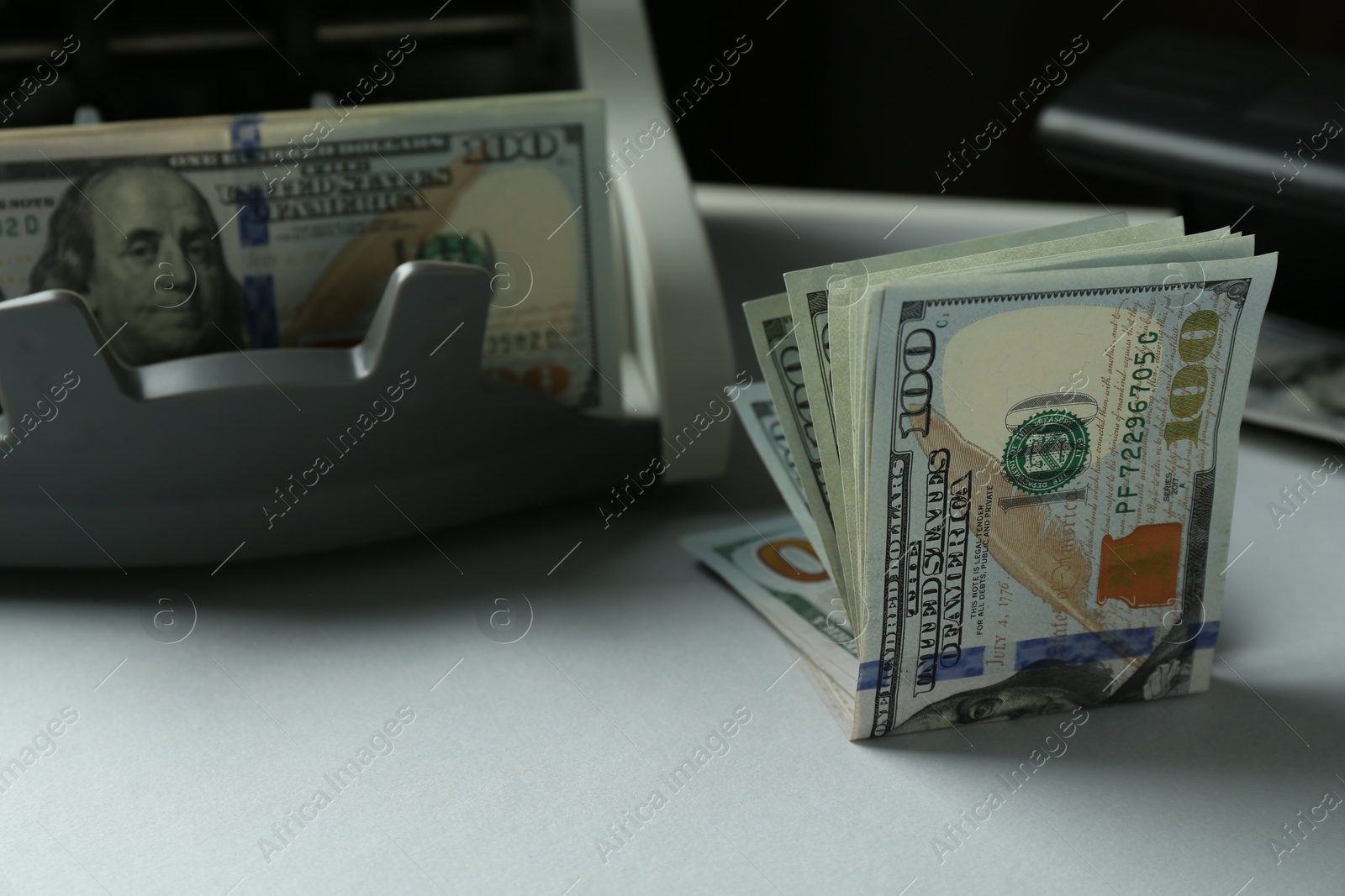 Photo of Dollar banknotes and money counter machine on light table, closeup