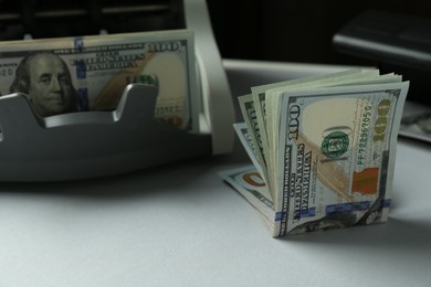 Dollar banknotes and money counter machine on light table, closeup