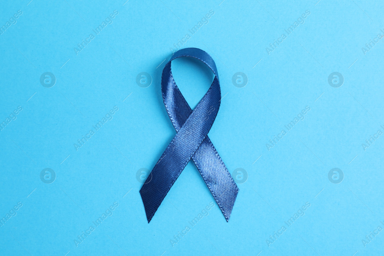 Photo of Dark blue ribbon on color background, top view. Prostate cancer awareness