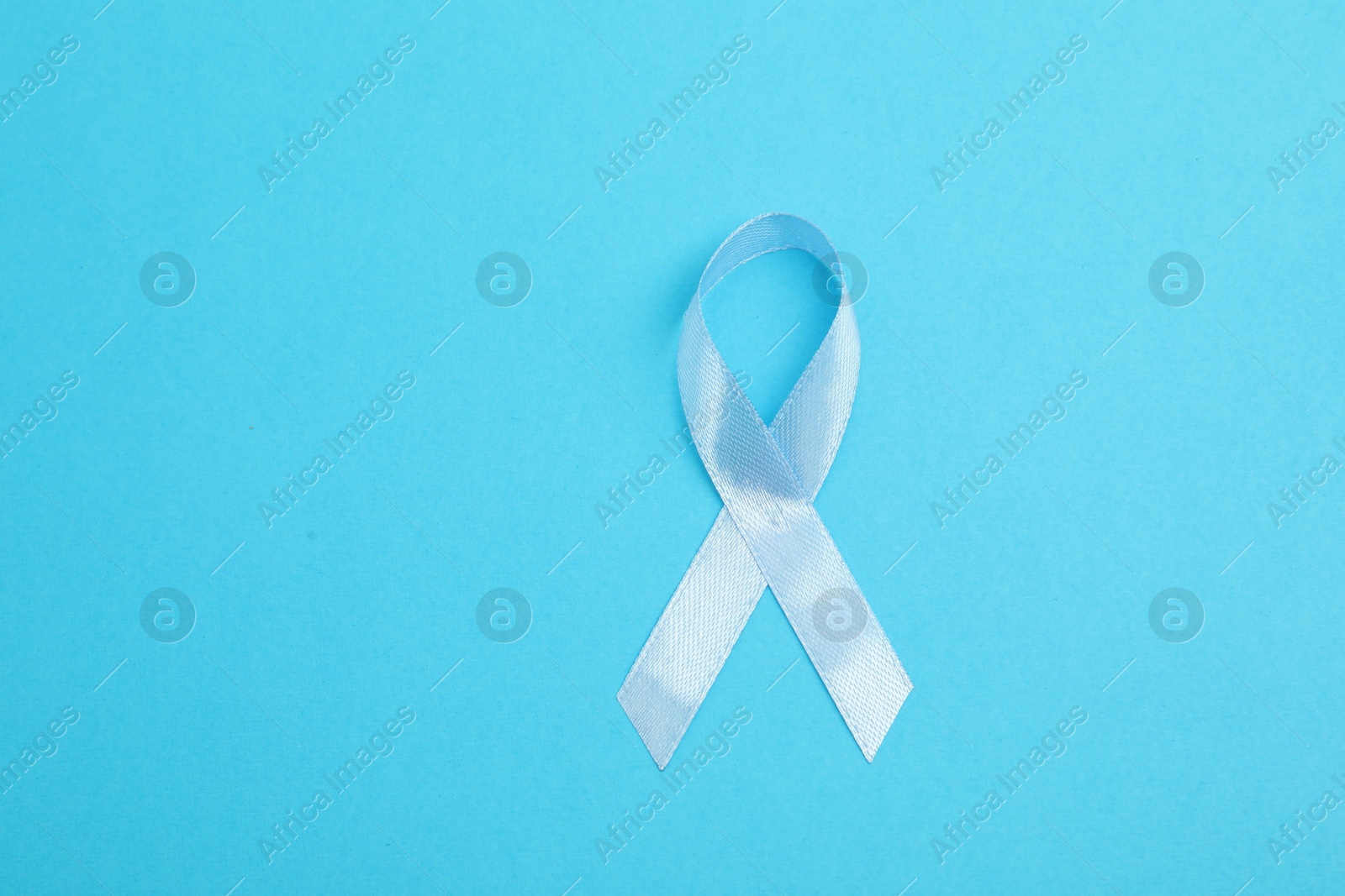 Photo of Light blue ribbon on color background, top view with space for text. Prostate cancer awareness