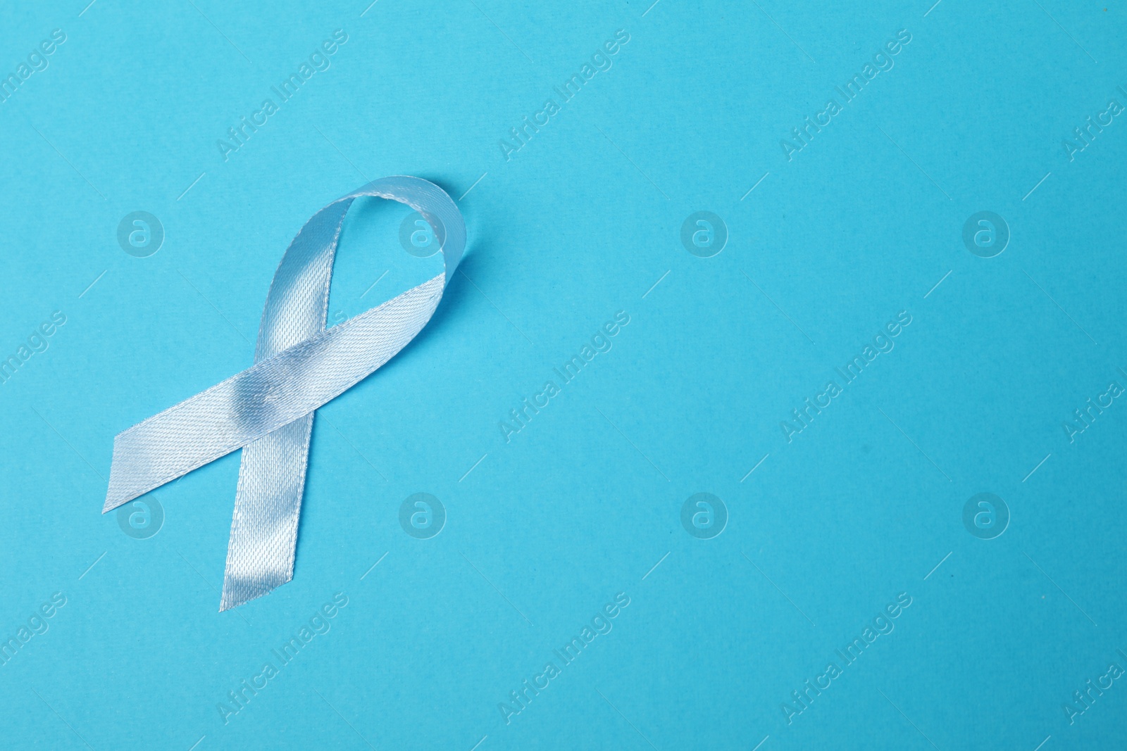 Photo of Light blue ribbon on color background, top view with space for text. Prostate cancer awareness