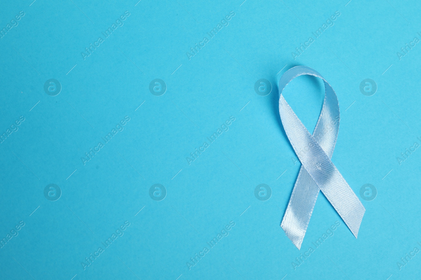 Photo of Light blue ribbon on color background, top view with space for text. Prostate cancer awareness