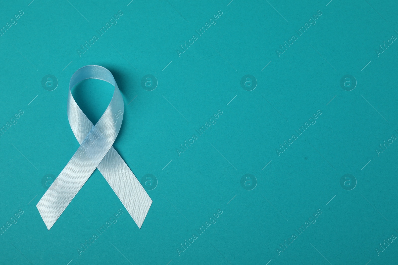 Photo of Light blue ribbon on teal background, top view with space for text. Prostate cancer awareness