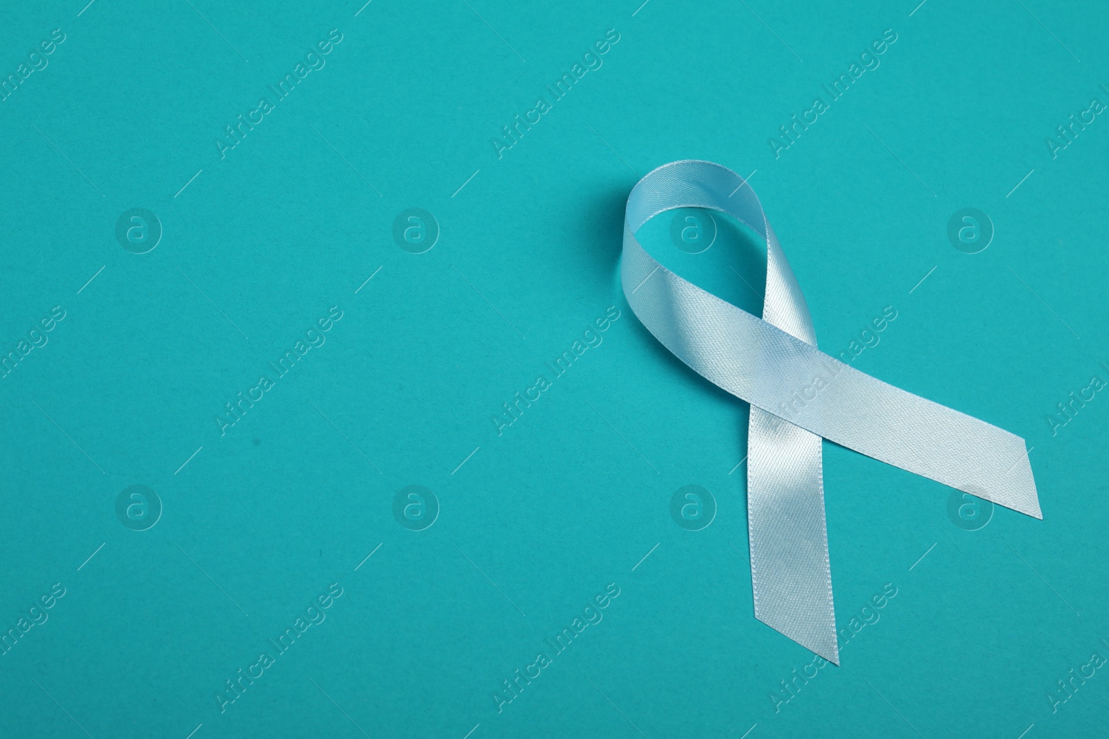 Photo of Prostate cancer awareness. Light blue ribbon on teal background, space for text