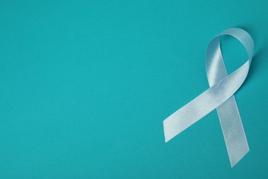 Photo of Light blue ribbon on teal background, top view with space for text. Prostate cancer awareness
