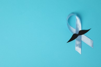 Photo of Light blue ribbon and fake mustache on color background, top view with space for text. Prostate cancer awareness