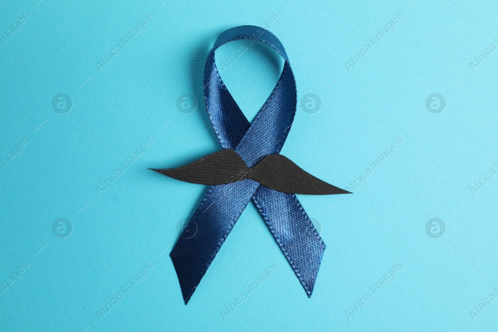 Photo of Dark blue ribbon and fake mustache on color background, top view. Prostate cancer awareness