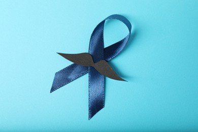 Photo of Dark blue ribbon and fake mustache on color background, top view. Prostate cancer awareness