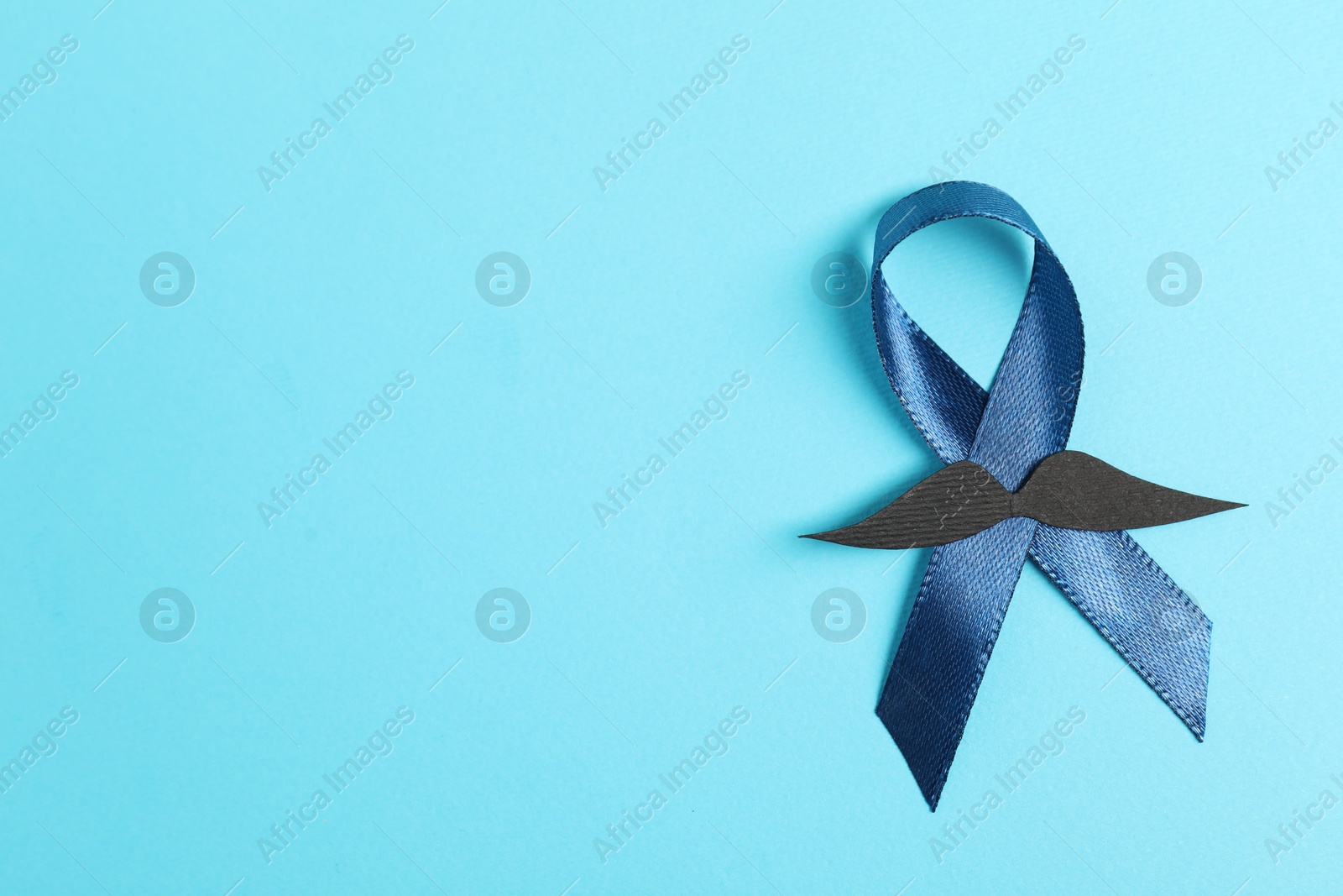 Photo of Dark blue ribbon and fake mustache on color background, top view with space for text. Prostate cancer awareness