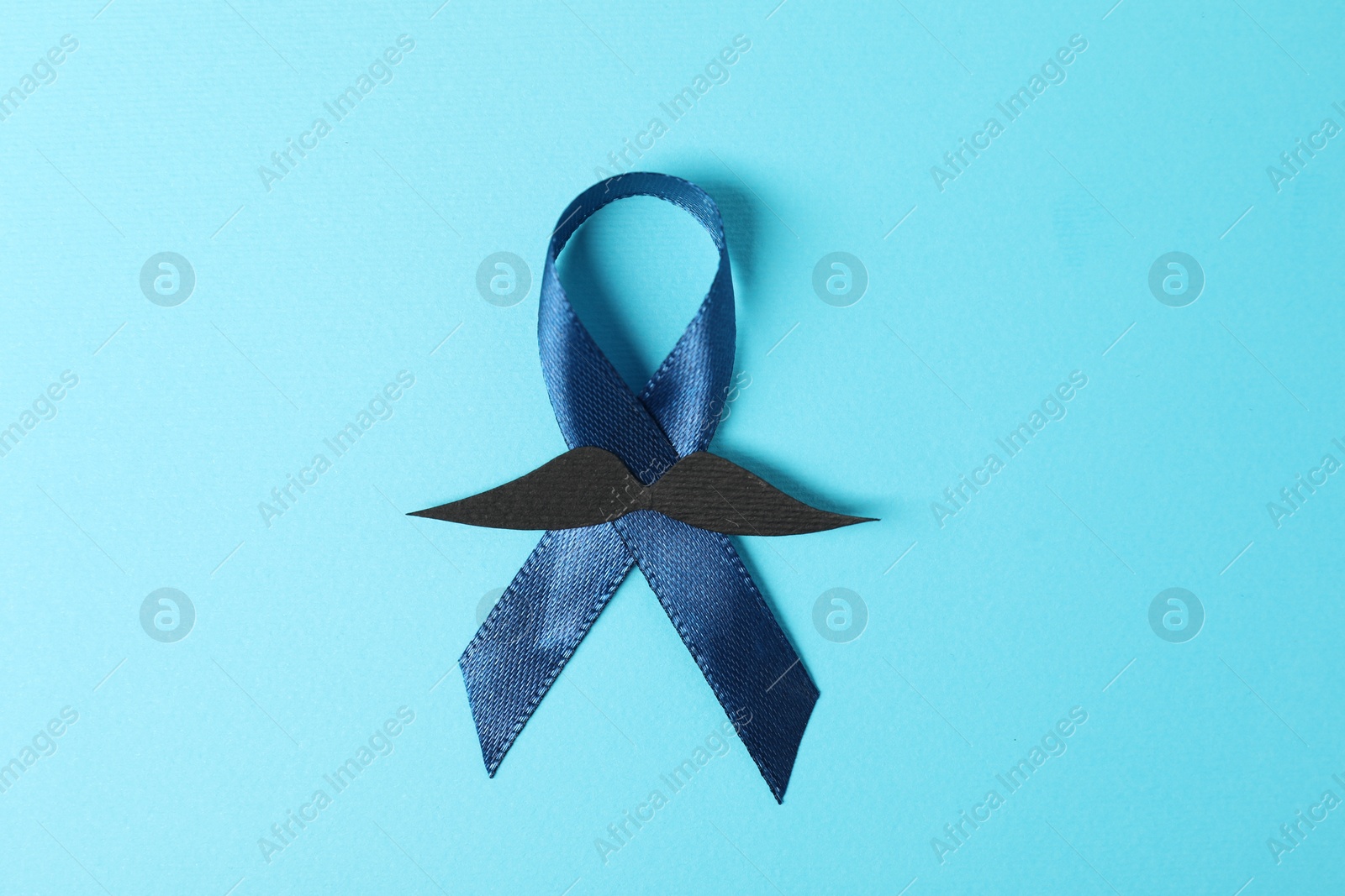 Photo of Dark blue ribbon and fake mustache on color background, top view. Prostate cancer awareness