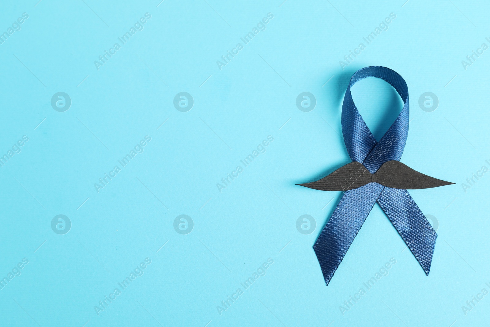 Photo of Dark blue ribbon and fake mustache on color background, top view with space for text. Prostate cancer awareness