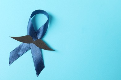 Photo of Dark blue ribbon and fake mustache on color background, top view with space for text. Prostate cancer awareness