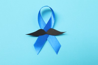 Photo of Blue ribbon and fake mustache on color background, top view. Prostate cancer awareness