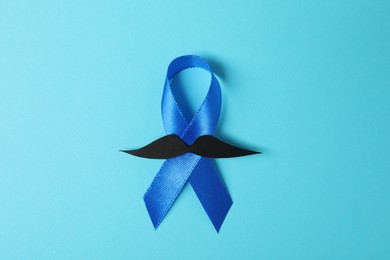 Photo of Blue ribbon and fake mustache on color background, top view. Prostate cancer awareness