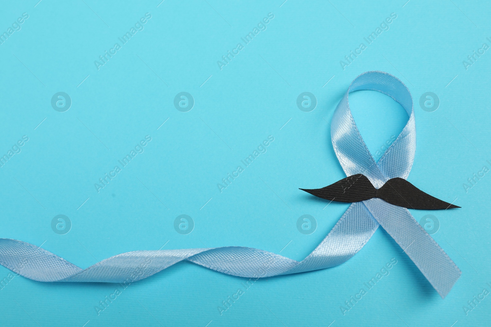 Photo of Light blue ribbon and fake mustache on color background, top view with space for text. Prostate cancer awareness