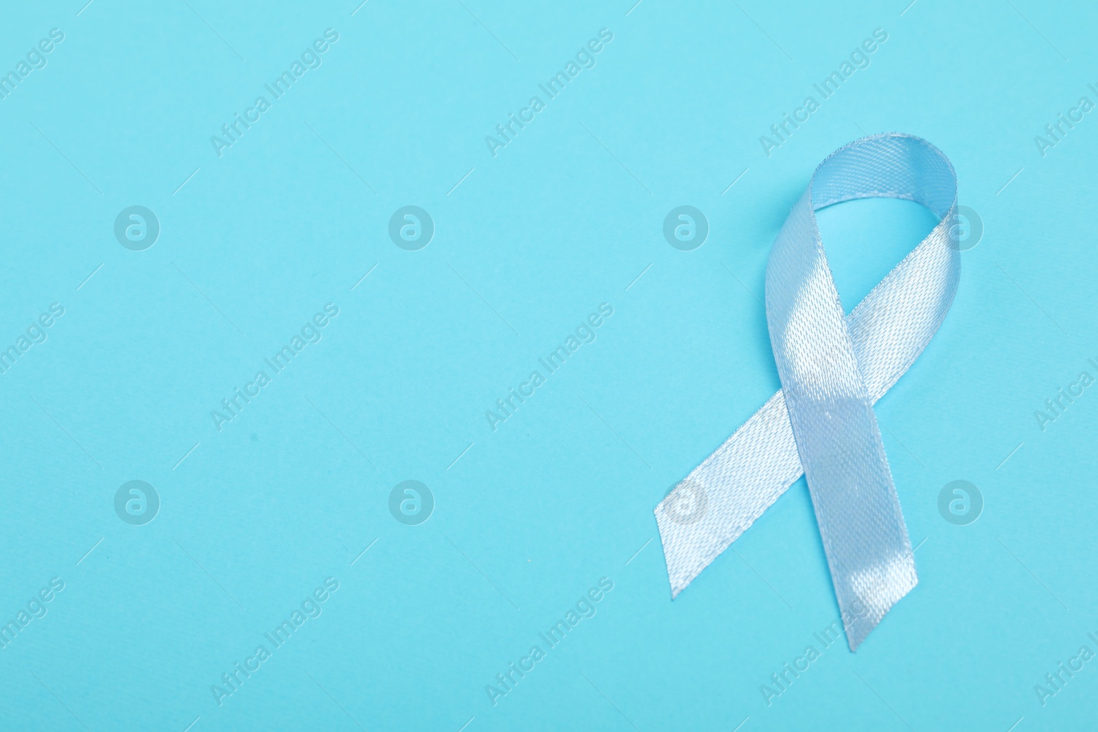 Photo of Light blue ribbon on color background, top view with space for text. Prostate cancer awareness