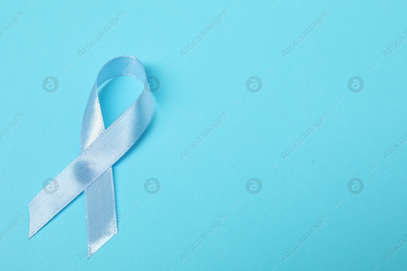 Photo of Light blue ribbon on color background, top view with space for text. Prostate cancer awareness