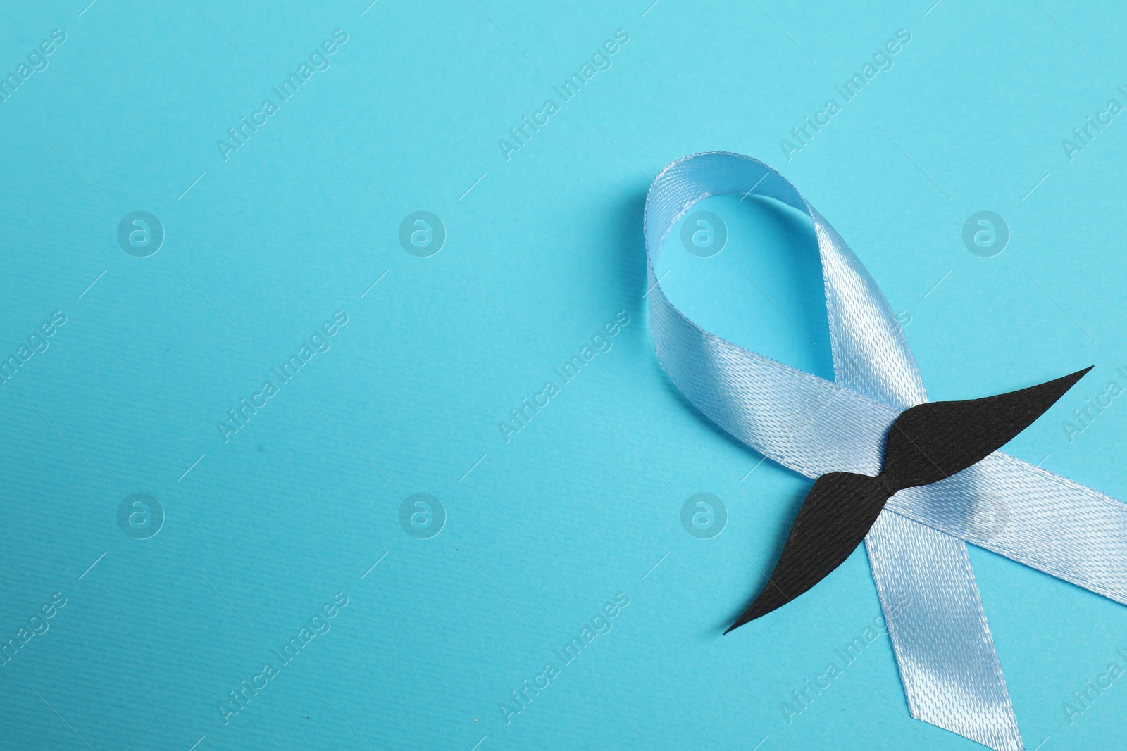 Photo of Light blue ribbon and fake mustache on color background, top view with space for text. Prostate cancer awareness