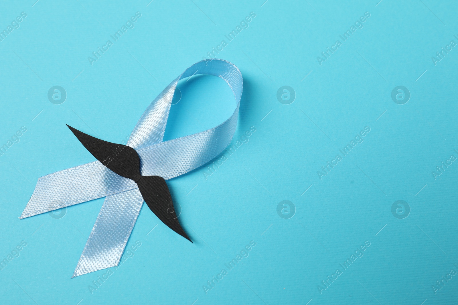 Photo of Light blue ribbon and fake mustache on color background, top view with space for text. Prostate cancer awareness