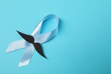Photo of Light blue ribbon and fake mustache on color background, top view with space for text. Prostate cancer awareness