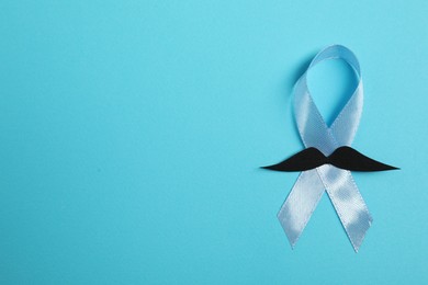 Photo of Light blue ribbon and fake mustache on color background, top view with space for text. Prostate cancer awareness