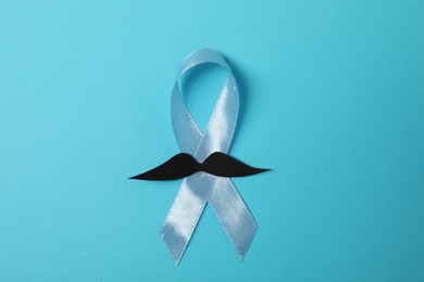 Photo of Light blue ribbon and fake mustache on color background, top view. Prostate cancer awareness