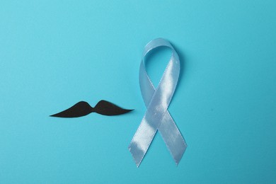 Light blue ribbon and fake mustache on color background, top view. Prostate cancer awareness