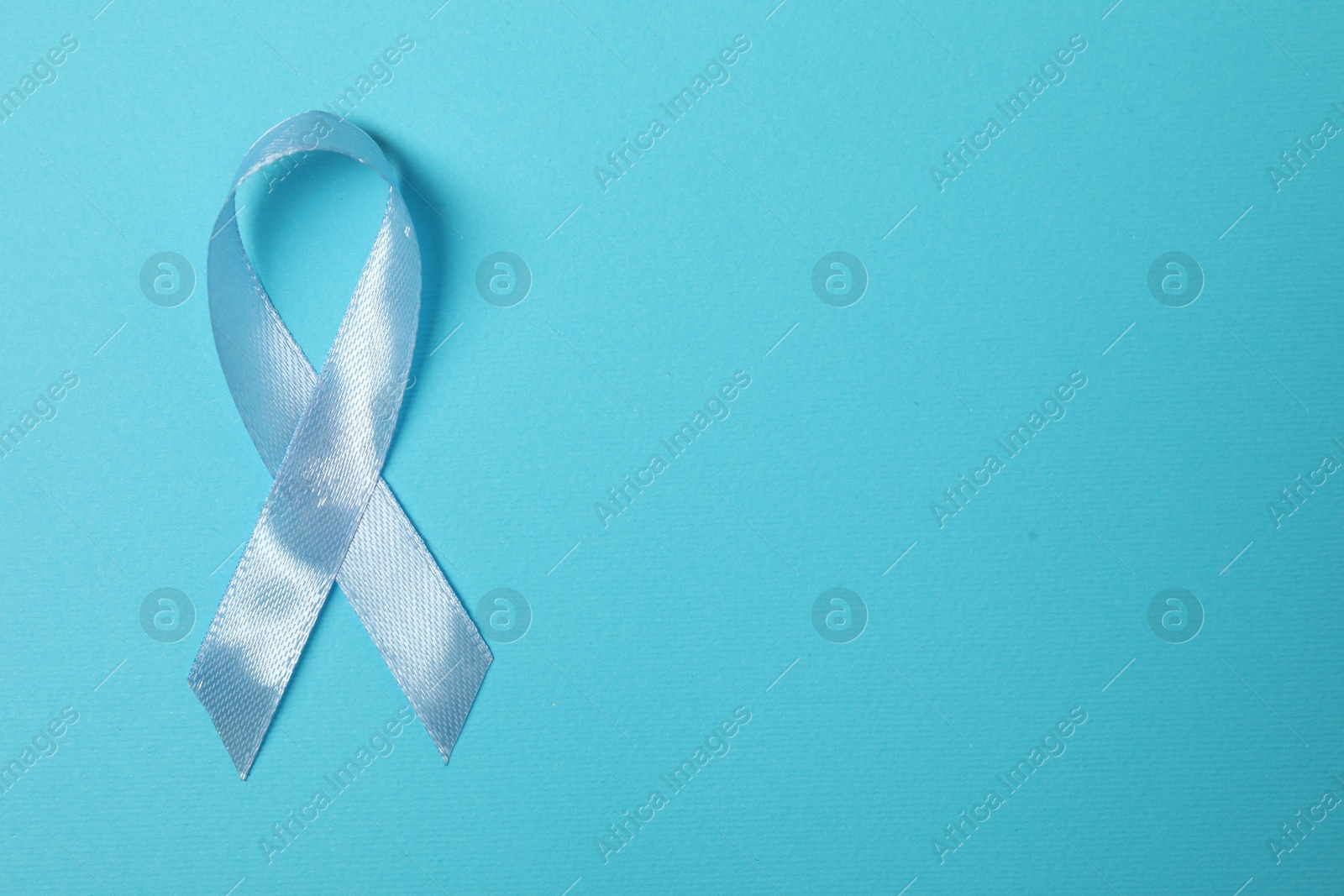 Photo of Light blue ribbon on color background, top view with space for text. Prostate cancer awareness