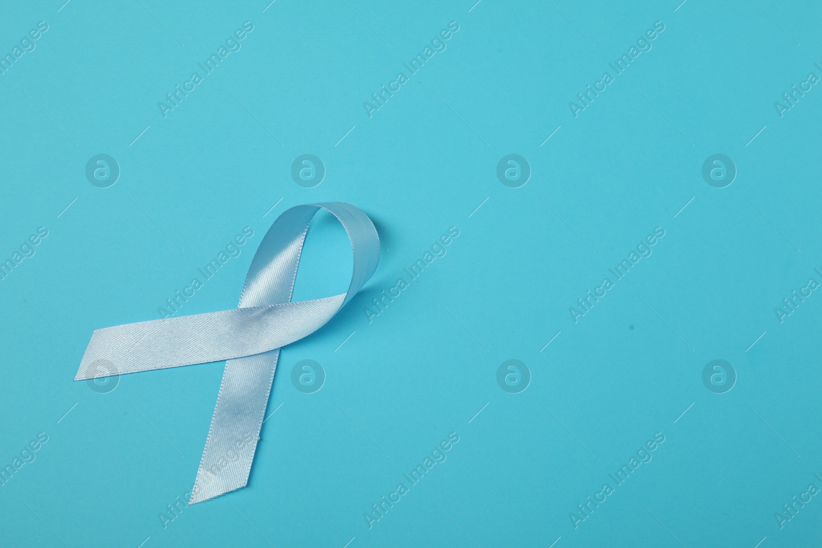 Photo of Light blue ribbon on color background, top view with space for text. Prostate cancer awareness