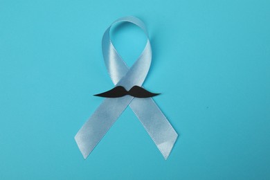 Photo of Light blue ribbon and fake mustache on color background, top view. Prostate cancer awareness