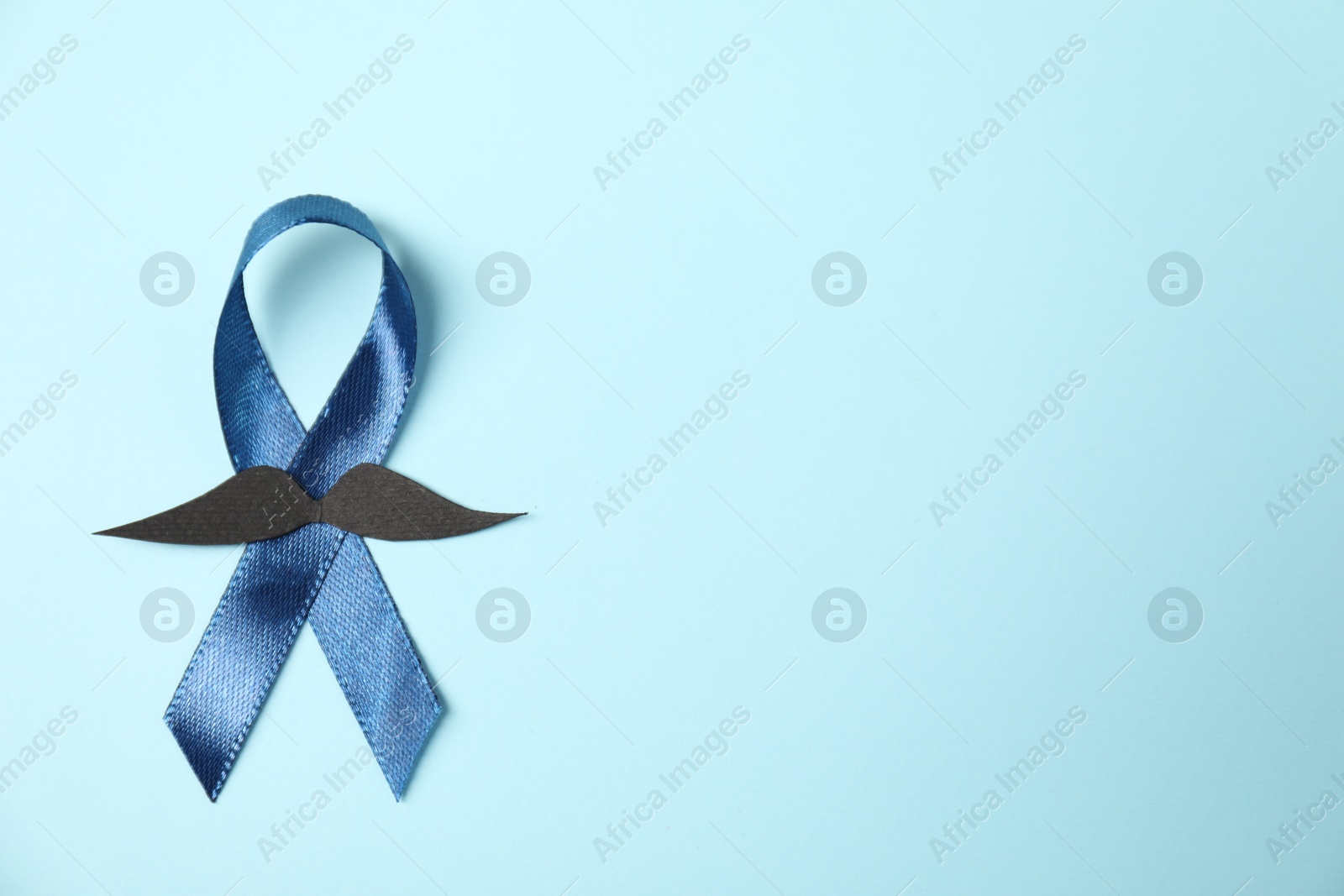 Photo of Dark blue ribbon and fake mustache on light background, top view with space for text. Prostate cancer awareness