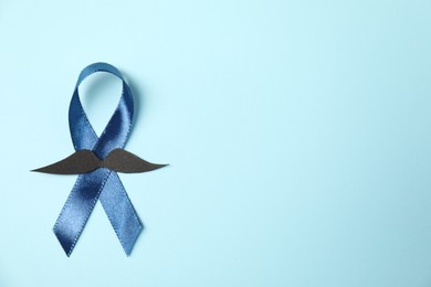 Photo of Dark blue ribbon and fake mustache on light background, top view with space for text. Prostate cancer awareness