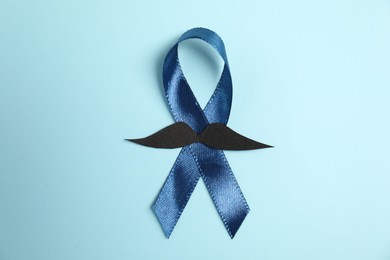 Photo of Dark blue ribbon and fake mustache on light background, top view. Prostate cancer awareness