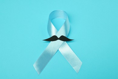 Photo of Light blue ribbon and fake mustache on color background, top view. Prostate cancer awareness
