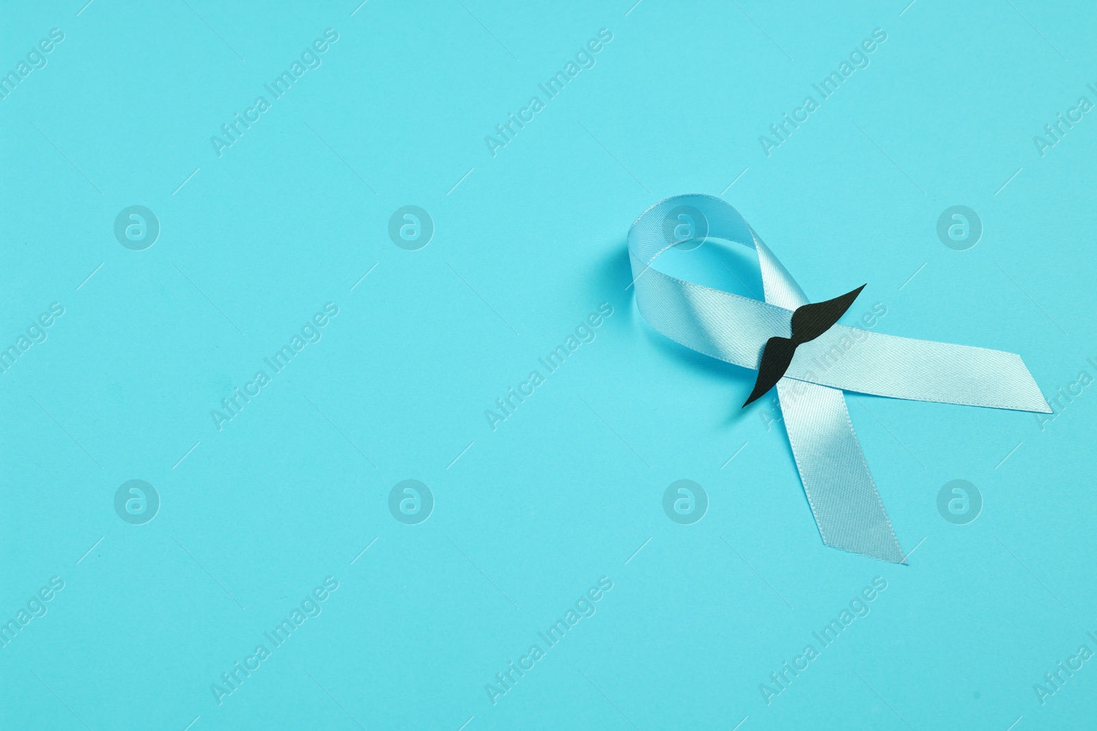 Photo of Light blue ribbon and fake mustache on color background, top view with space for text. Prostate cancer awareness