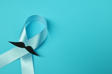 Photo of Prostate cancer awareness. Light blue ribbon and fake mustache on color background, closeup. Space for text