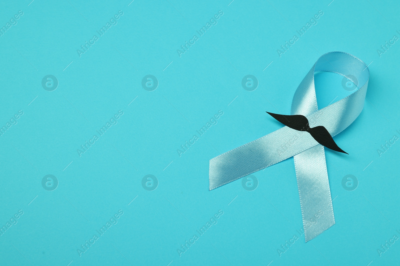 Photo of Light blue ribbon and fake mustache on color background, top view with space for text. Prostate cancer awareness