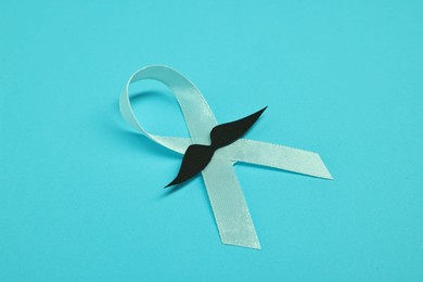 Photo of Light blue ribbon and fake mustache on color background, closeup. Prostate cancer awareness