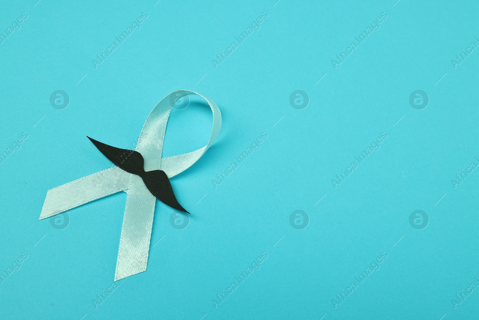 Photo of Light blue ribbon and fake mustache on color background, top view with space for text. Prostate cancer awareness