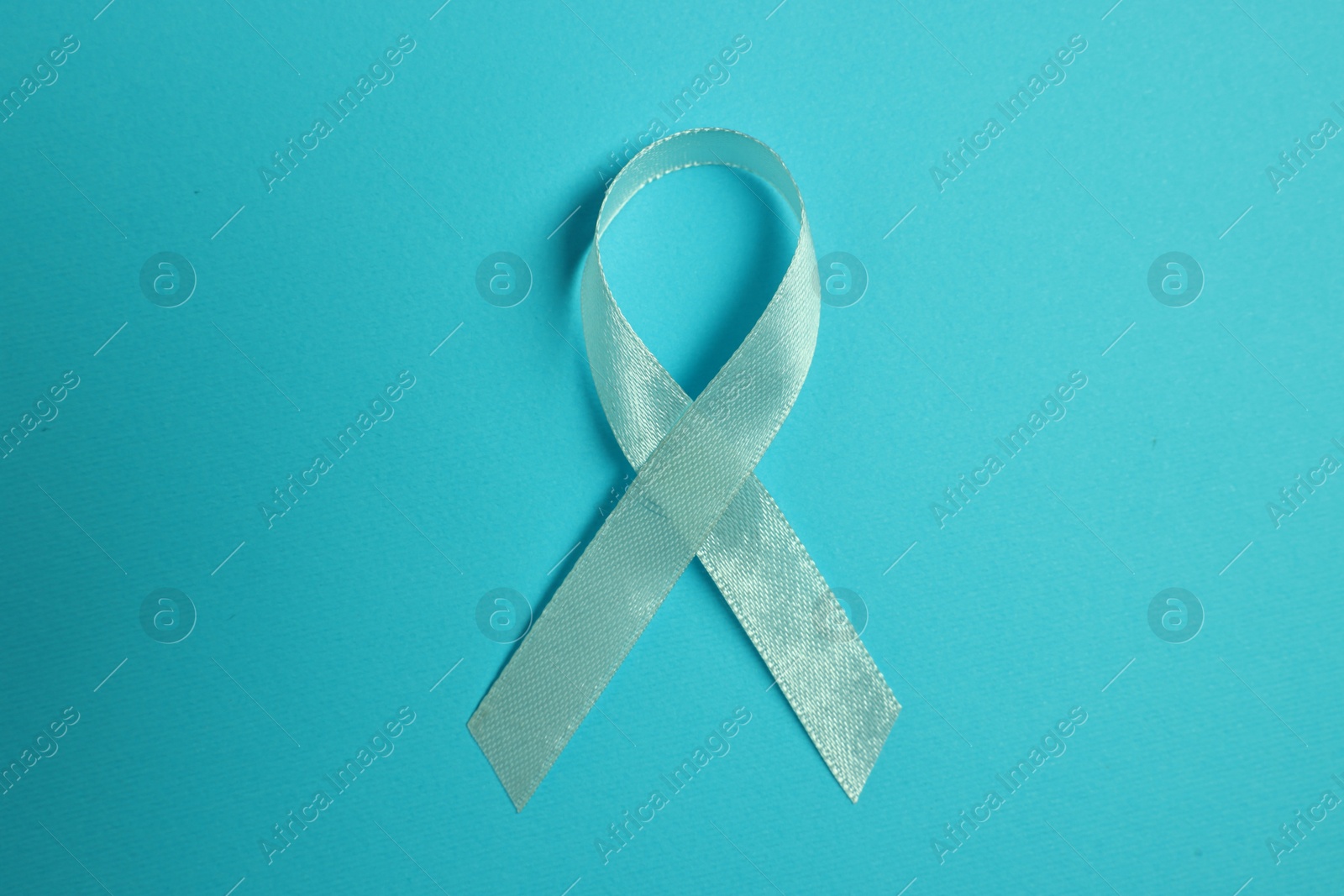 Photo of Light blue ribbon on color background, top view. Prostate cancer awareness