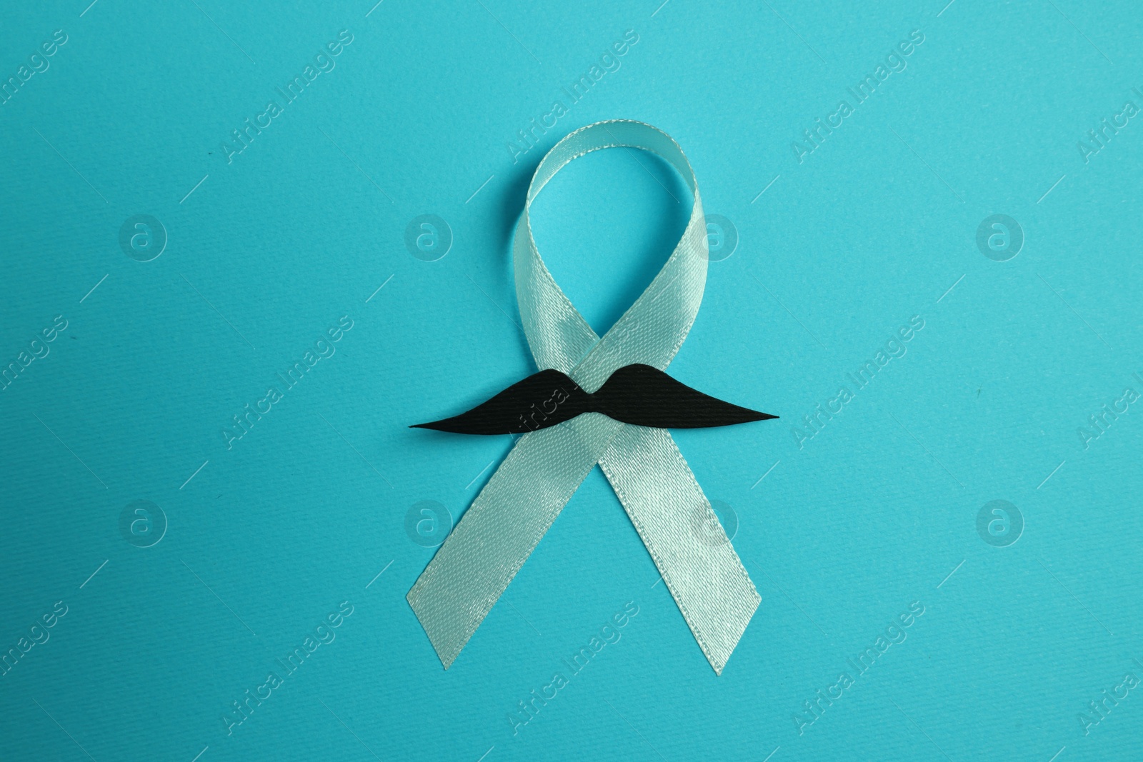 Photo of Light blue ribbon and fake mustache on color background, top view. Prostate cancer awareness