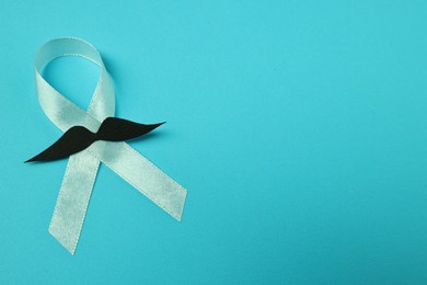 Photo of Light blue ribbon and fake mustache on color background, space for text. Prostate cancer awareness