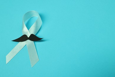 Photo of Light blue ribbon and fake mustache on color background, space for text. Prostate cancer awareness