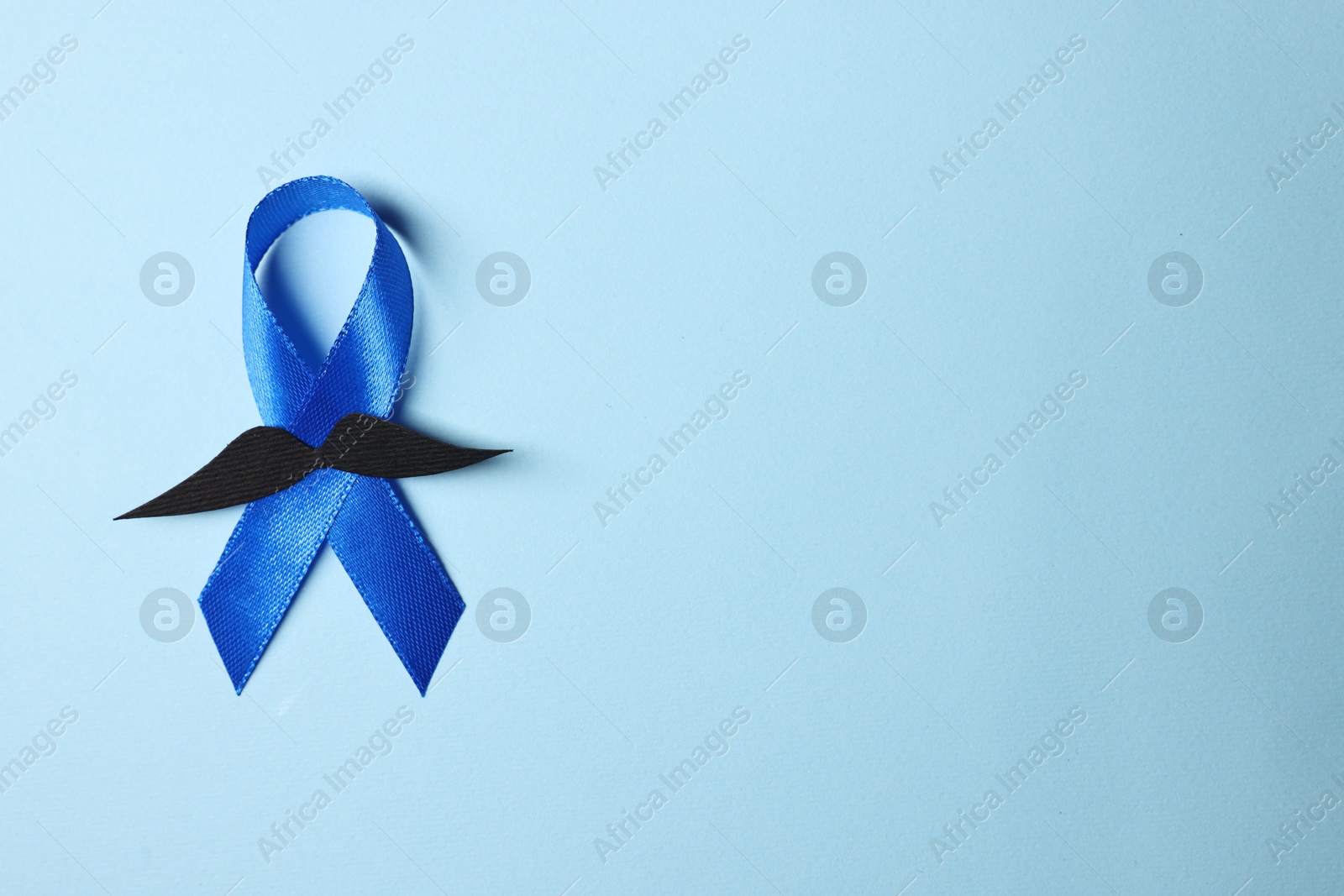 Photo of Blue ribbon and fake mustache on light background, top view with space for text. Prostate cancer awareness