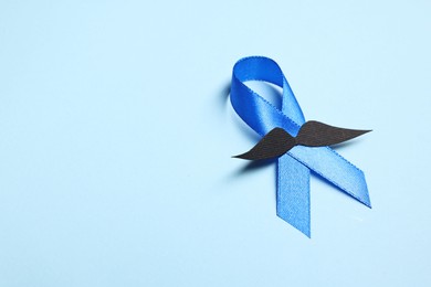 Photo of Blue ribbon and fake mustache on light background, space for text. Prostate cancer awareness